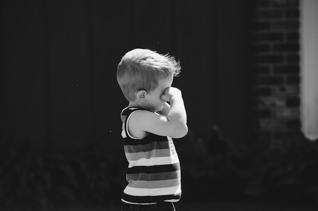 a black and white image of a little boy rubbing his eyes