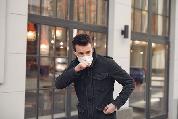 A man wearing a face mask coughs into his hand